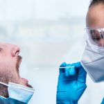 Female doctor with facemask swabbing patient's throat